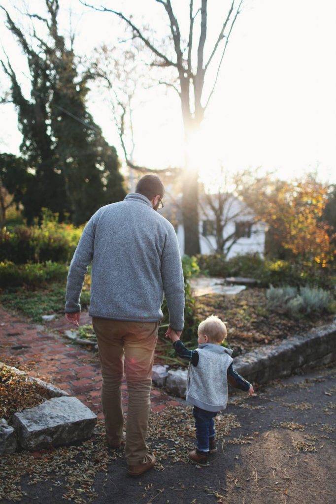 man holding hands with baby while walking through pathway facing sunlight